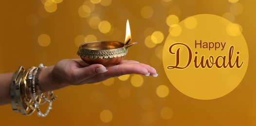 Image of Happy Diwali greeting card, Hindu festival of lights. Woman holding lit diya lamp on color background with blurred lights, closeup. Banner design