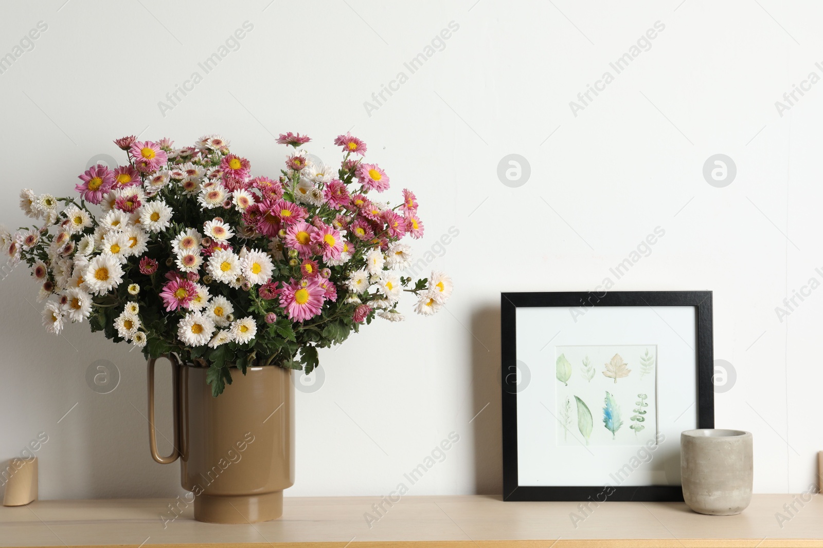 Photo of Vase with beautiful flowers and other decor on wooden shelf near white wall