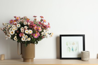 Photo of Vase with beautiful flowers and other decor on wooden shelf near white wall