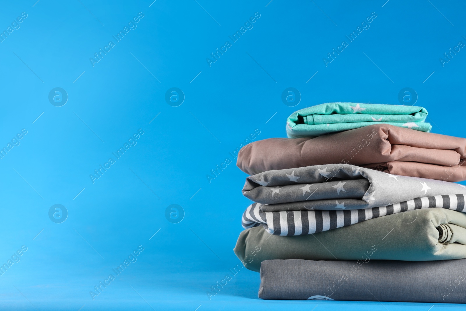 Photo of Stack of clean bed sheets on blue background. Space for text