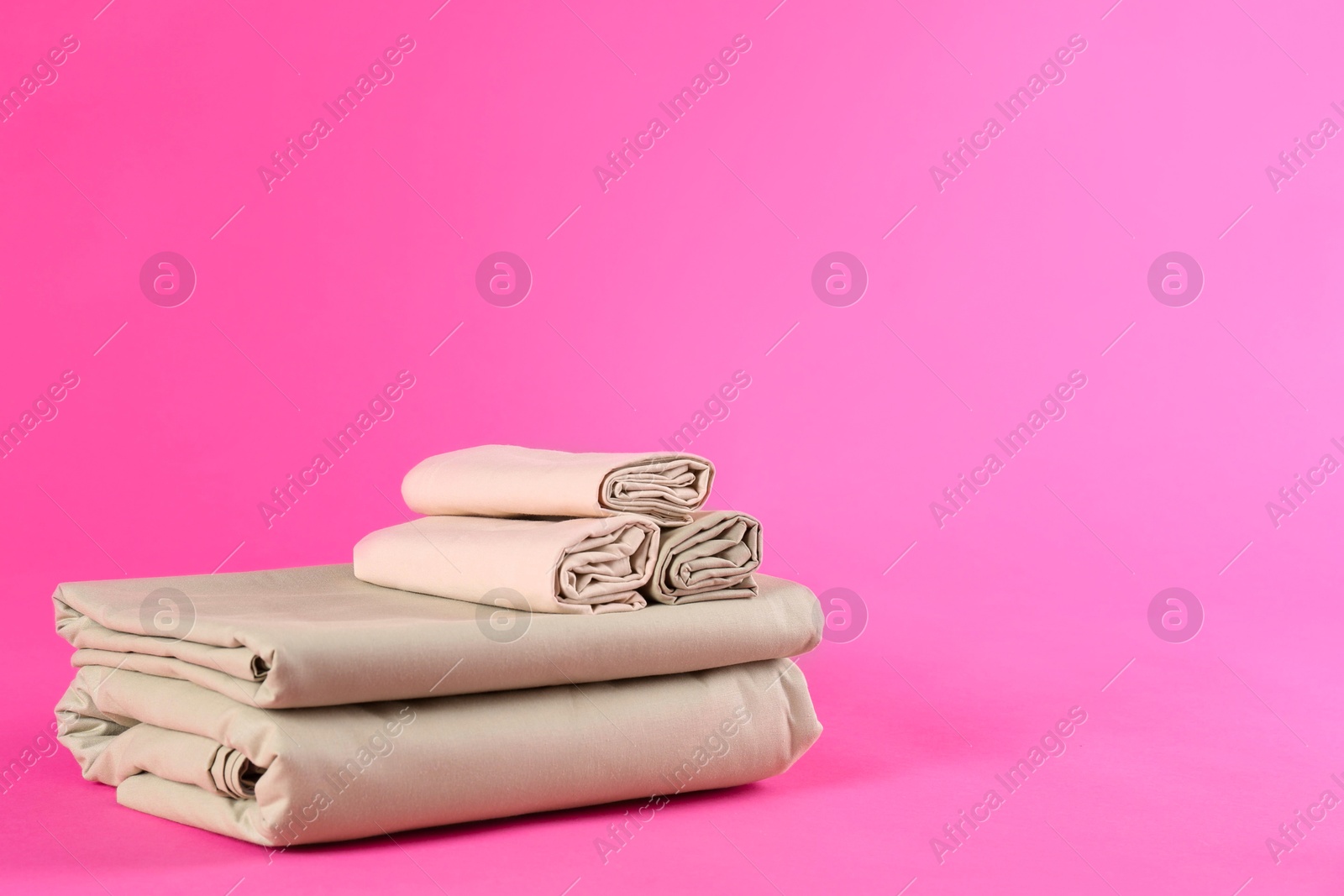 Photo of Stack of clean bed sheets on pink background. Space for text