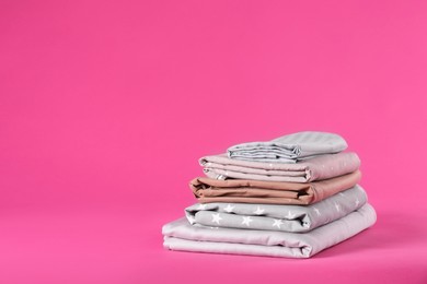 Photo of Stack of clean bed sheets on pink background. Space for text