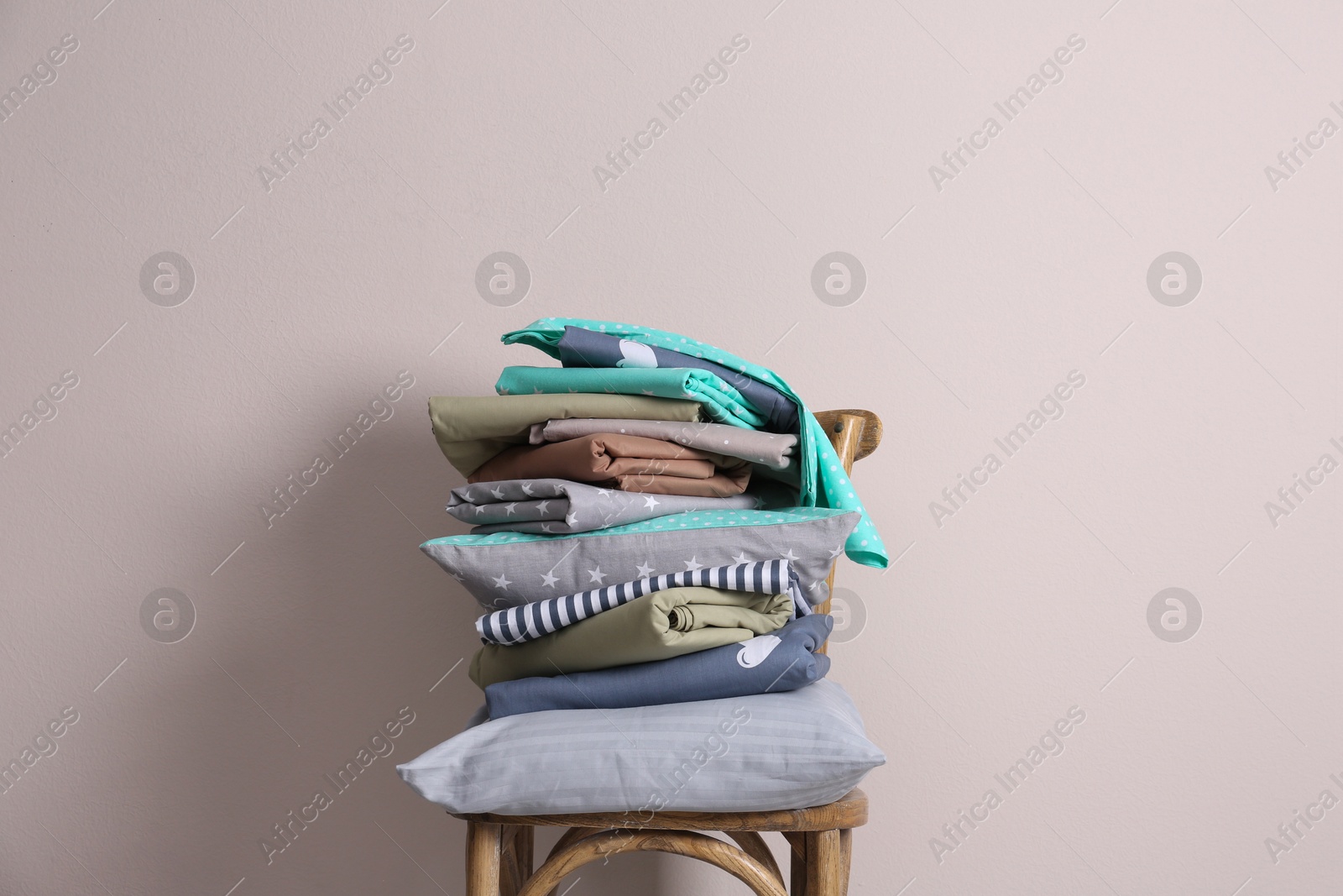 Photo of Stack of clean bed sheets and pillow on chair near beige wall