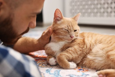 Photo of Man petting cute ginger cat on floor at home, closeup