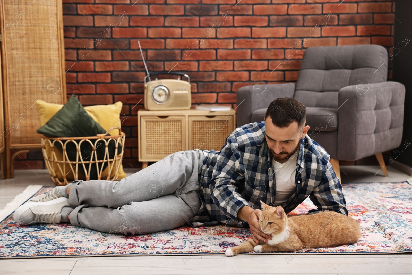 Photo of Man petting cute ginger cat on floor at home