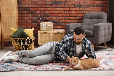 Man petting cute ginger cat on floor at home