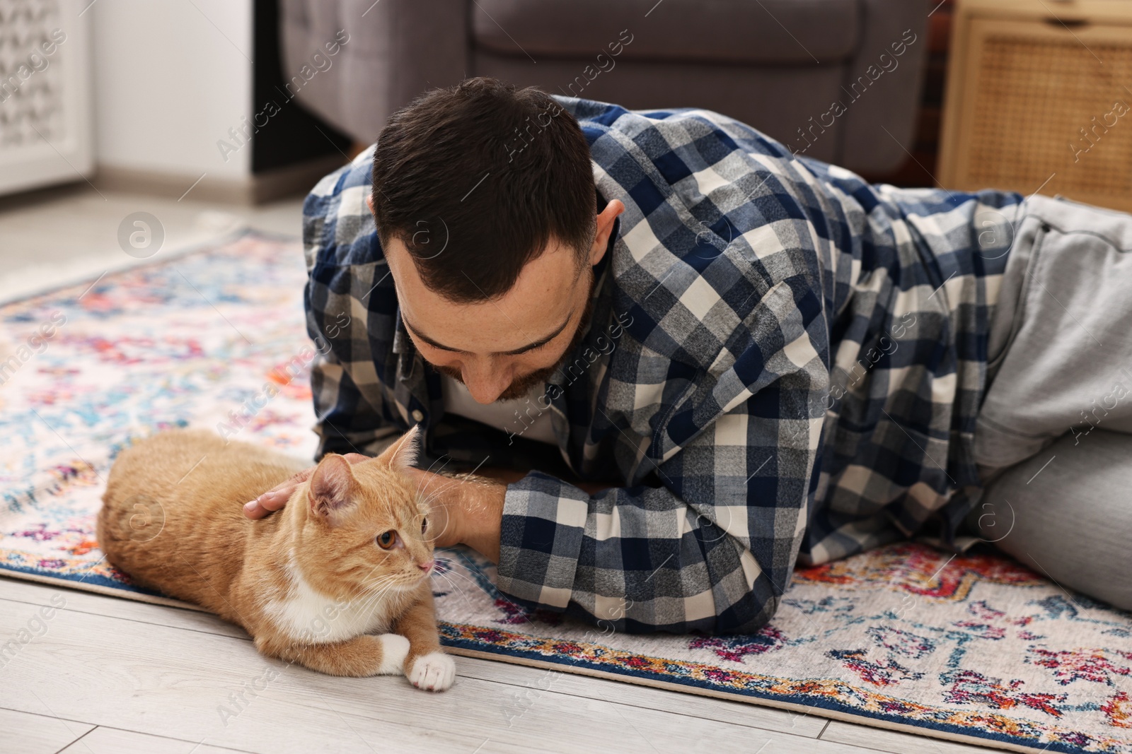 Photo of Man petting cute ginger cat on floor at home