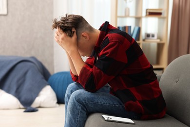 Photo of Loneliness concept. Sad teenage boy with smartphone on sofa at home