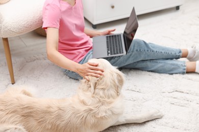 Online pet shop. Woman with laptop making order for cute Golden Retriever dog on rug at home, closeup