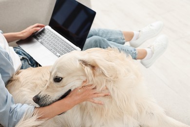 Online pet shop. Woman with laptop making order for cute Golden Retriever dog at home, closeup