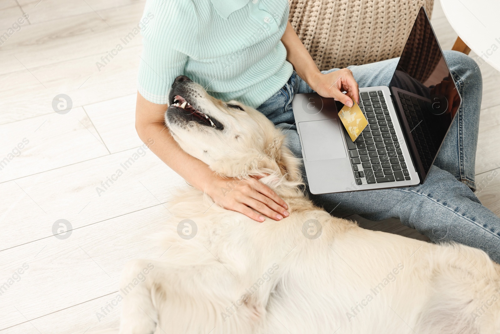 Photo of Online pet shop. Woman with laptop, credit card and cute Golden Retriever dog making order at home, closeup