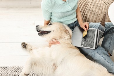 Online pet shop. Woman with laptop, credit card and cute Golden Retriever dog making order at home, closeup