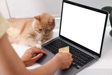 Online pet shop. Woman with laptop, credit card and cute cat making order at home, closeup