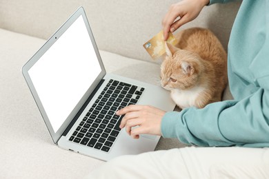 Online pet shop. Woman with laptop, credit card and cute cat making order on sofa at home, closeup