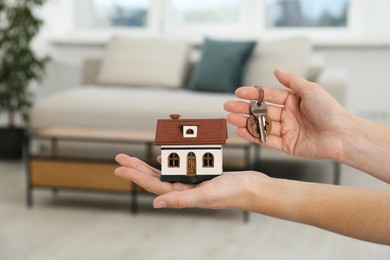 Photo of Woman holding key with keychain and house model indoors, closeup