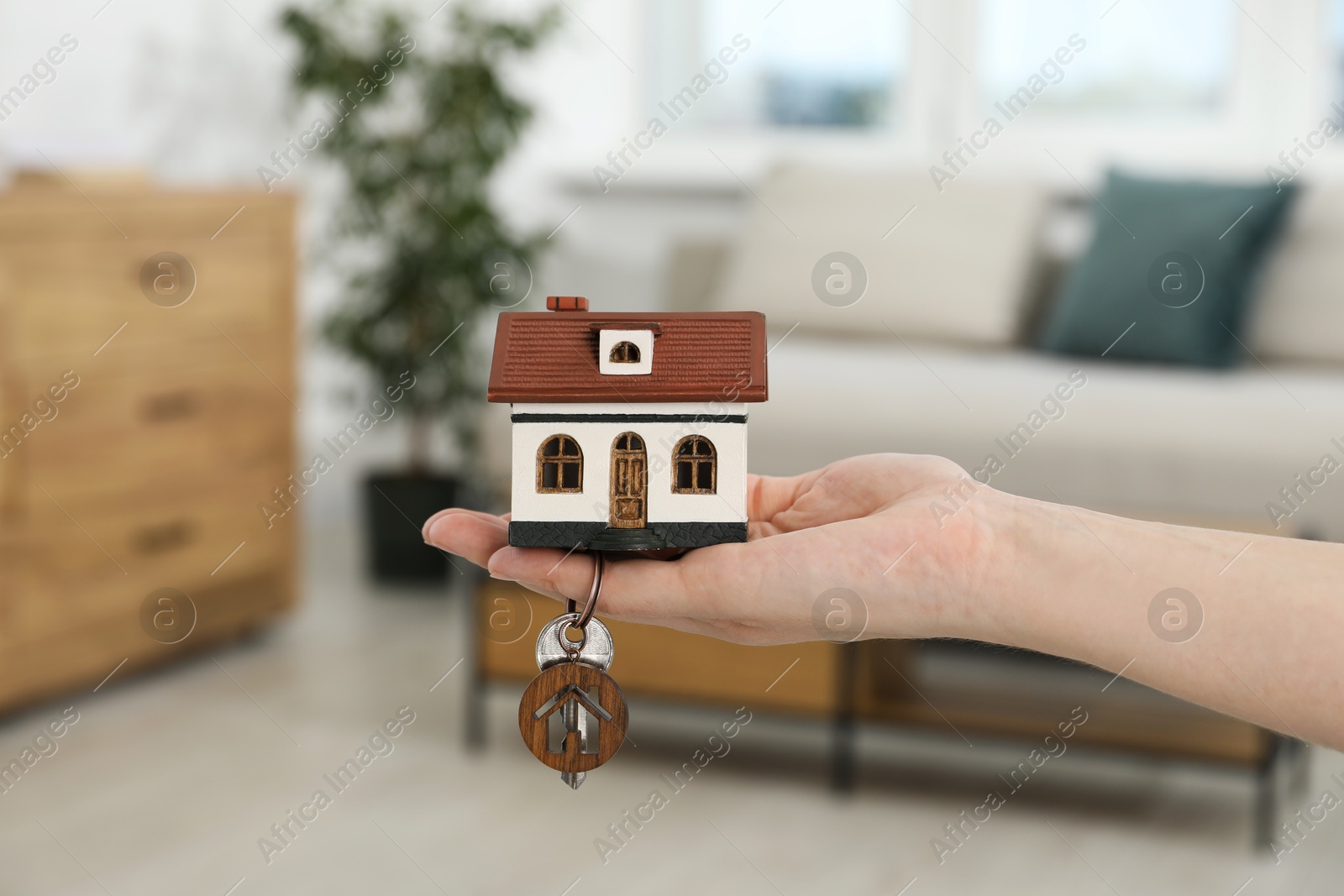 Photo of Woman holding key with keychain and house model indoors, closeup