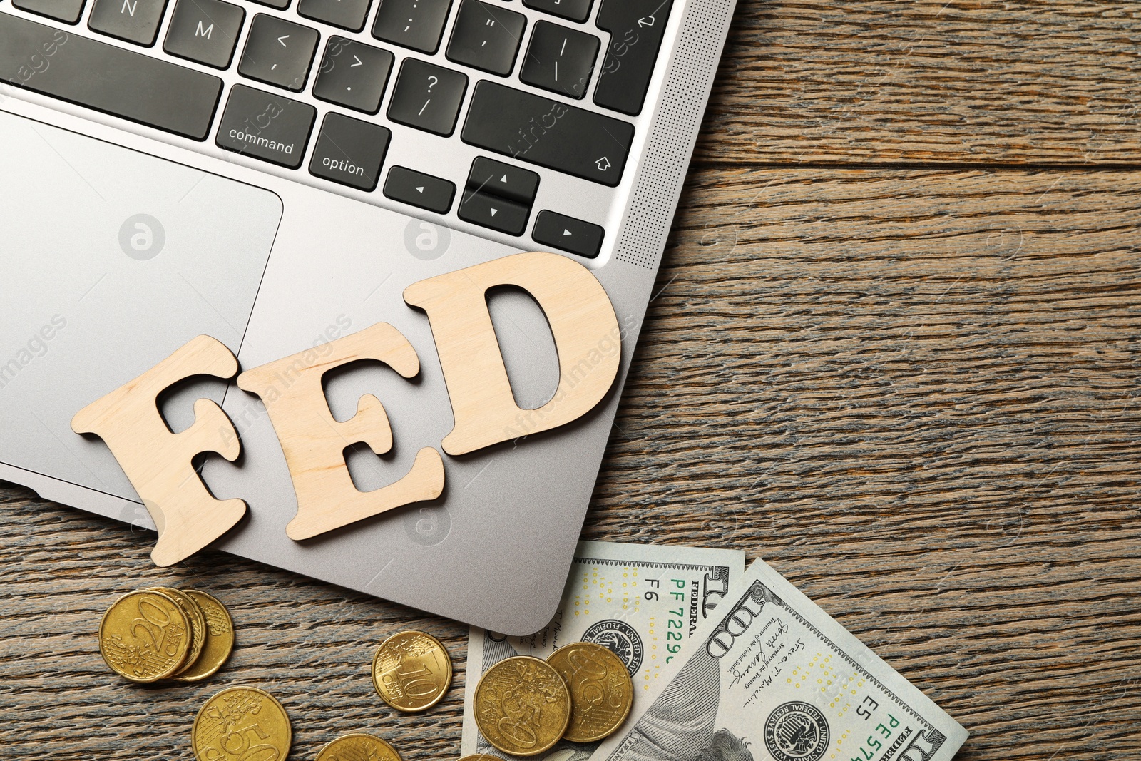 Photo of Letters Fed (Federal Reserve System), coins, dollar banknotes and laptop on wooden table, flat lay