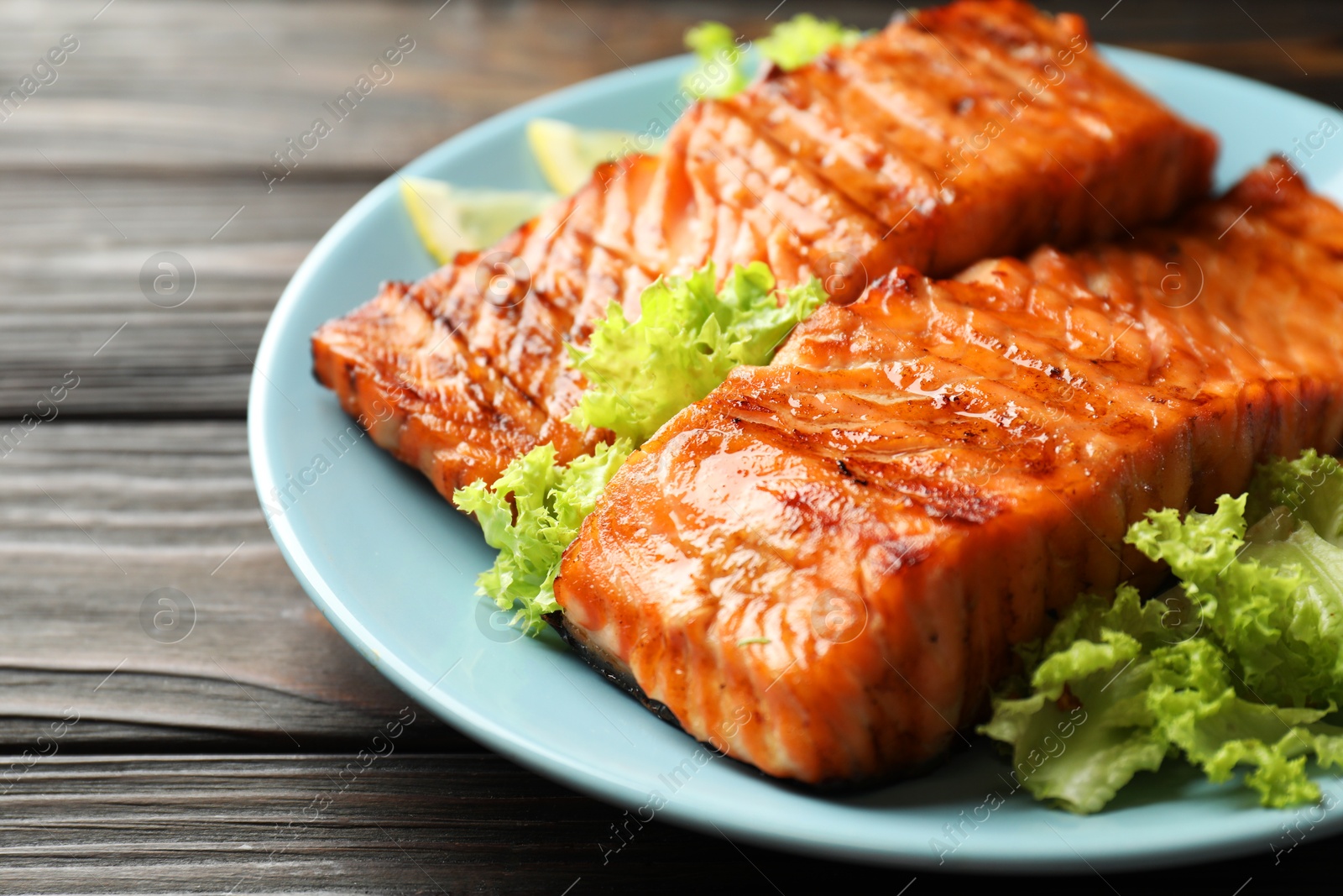 Photo of Delicious grilled salmon fillets with lettuce on wooden table, closeup