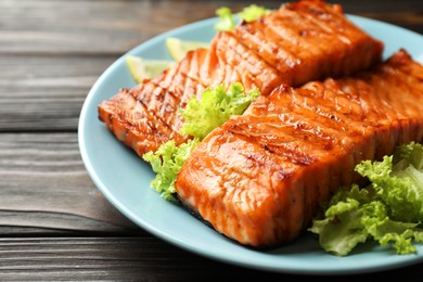 Photo of Delicious grilled salmon fillets with lettuce on wooden table, closeup