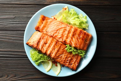 Photo of Delicious grilled salmon fillets with lettuce and lemon on wooden table, top view