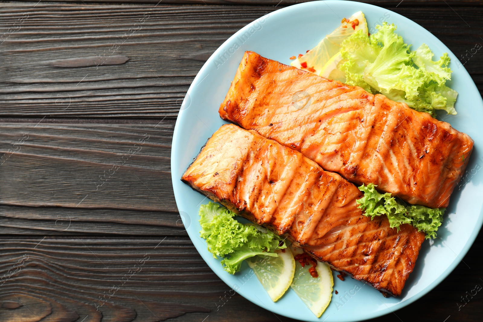 Photo of Delicious grilled salmon fillets with lettuce and lemon on wooden table, top view. Space for text