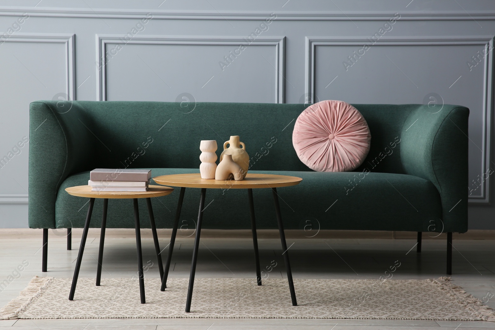 Photo of Stylish sofa with cushion, books and decor elements on nesting tables in room