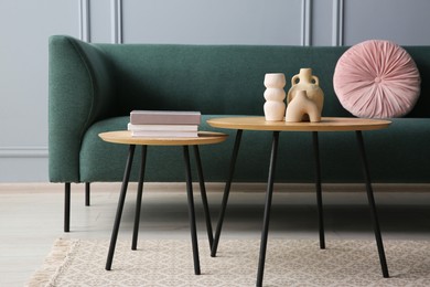 Photo of Stylish sofa with cushion, books and decor elements on nesting tables in room