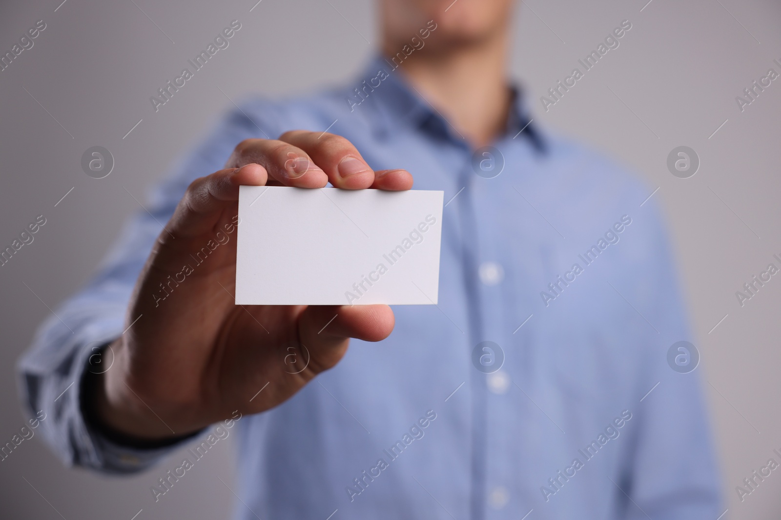 Photo of Man holding blank business card on grey background, closeup. Mockup for design