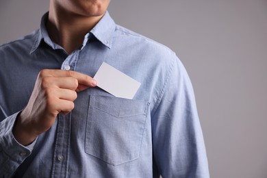 Man taking blank business card from pocket of his jacket on grey background, closeup. Mockup for design