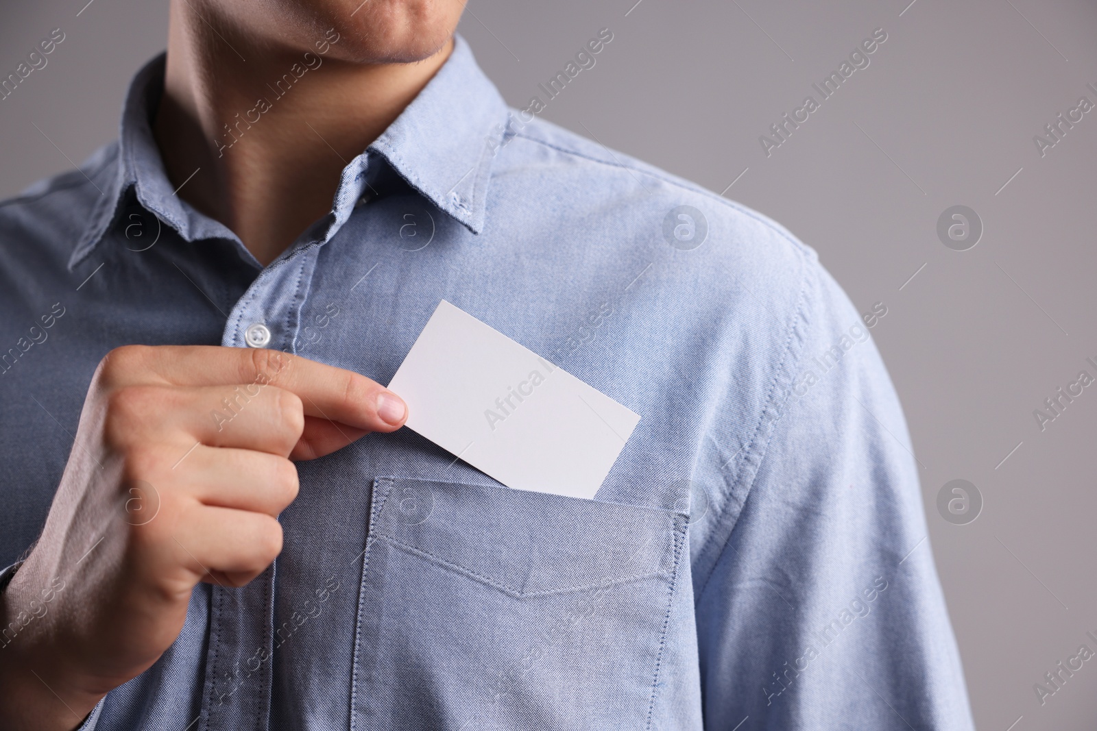 Photo of Man taking blank business card from pocket of his jacket on grey background, closeup. Mockup for design