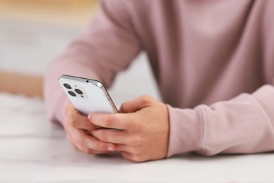 Man using smartphone at white table indoors, closeup