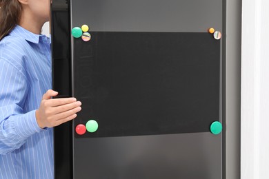 Woman opening refrigerator with blank magnetic board in kitchen, closeup