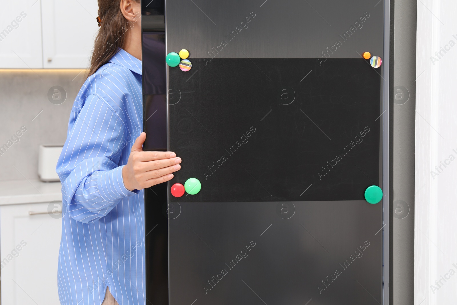 Photo of Woman opening refrigerator with blank magnetic board in kitchen, closeup