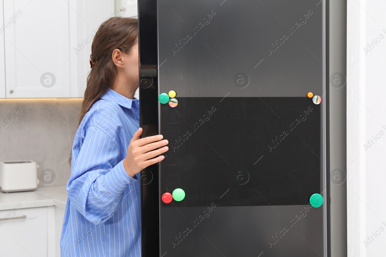 Photo of Woman opening refrigerator with blank magnetic board in kitchen, closeup