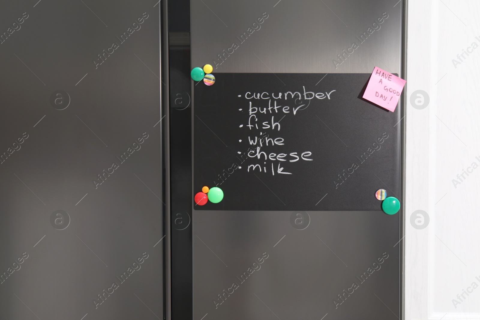 Photo of Magnetic board with shopping list and note on refrigerator in kitchen