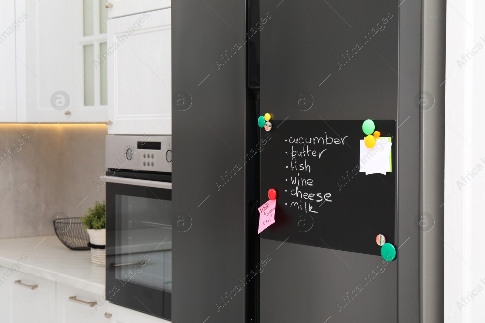 Photo of Magnetic board with shopping list and notes on refrigerator in kitchen