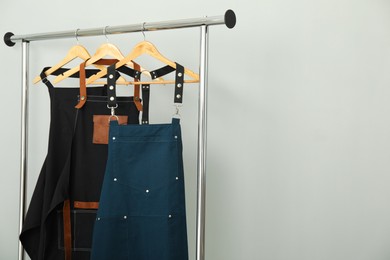 Photo of Aprons on clothing rack near light grey wall, space for text