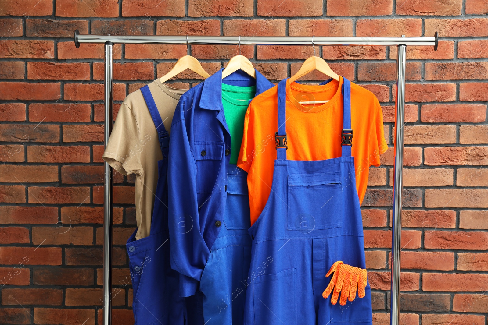 Photo of Different workers' uniforms on clothing rack near brick wall