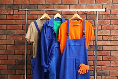 Different workers' uniforms on clothing rack near brick wall