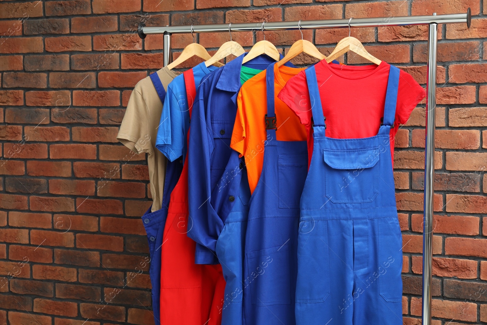 Photo of Different workers' uniforms on clothing rack near brick wall