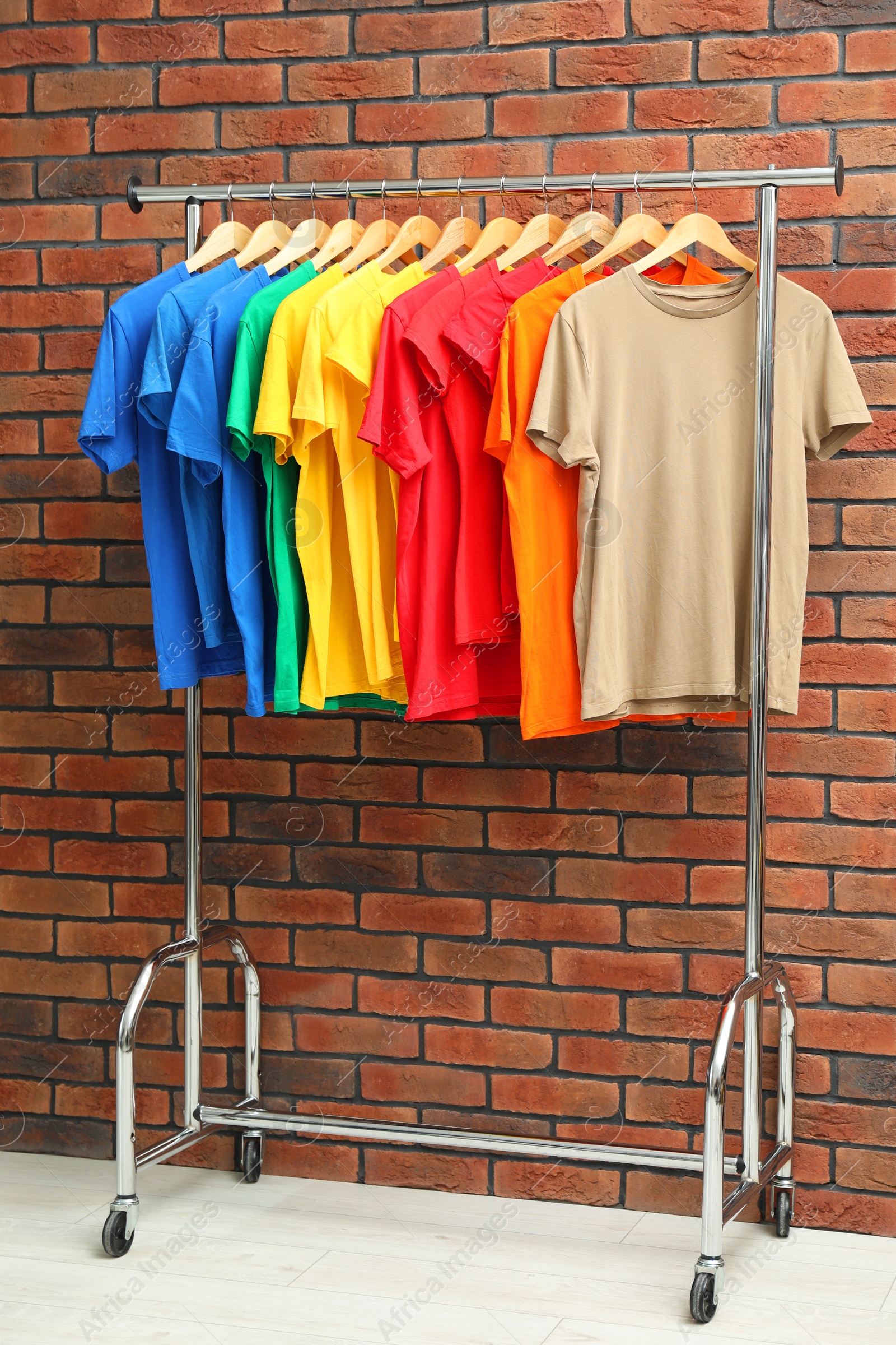 Photo of Many colorful t-shirts on clothing rack near brick wall