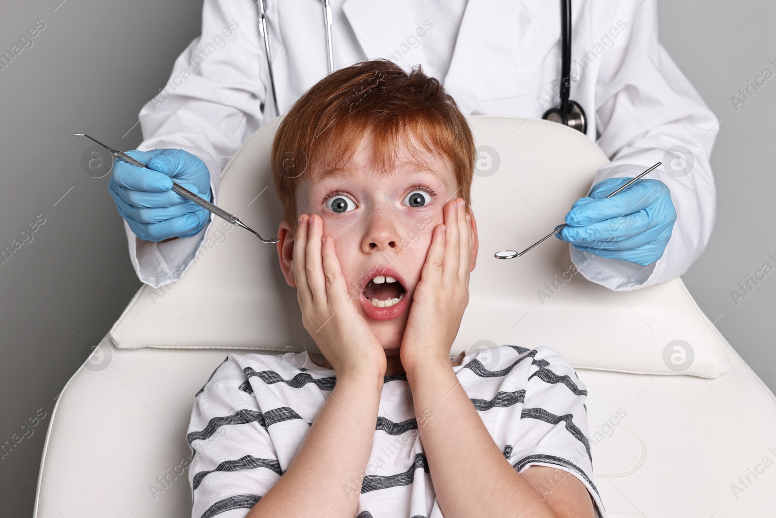 Photo of Dental phobia. Dentist working with scared little boy on grey background