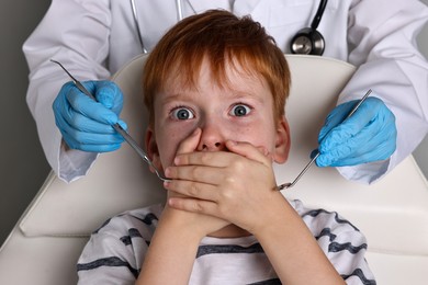 Dental phobia. Dentist working with scared little boy on grey background