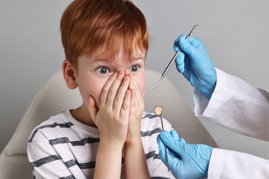 Photo of Dental phobia. Dentist working with scared little boy on grey background