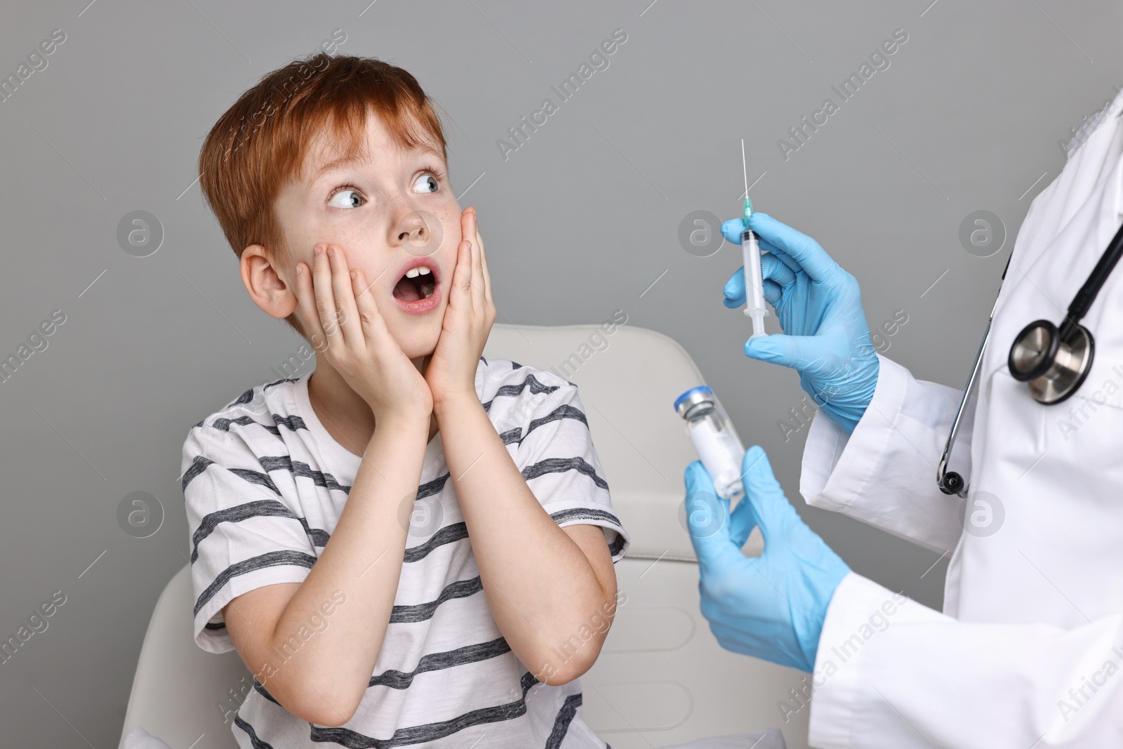 Photo of Dental phobia. Dentist with syringe and vial near scared boy on grey background