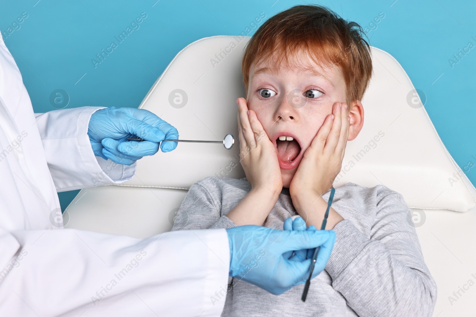 Photo of Dental phobia. Dentist working with scared little boy on light blue background