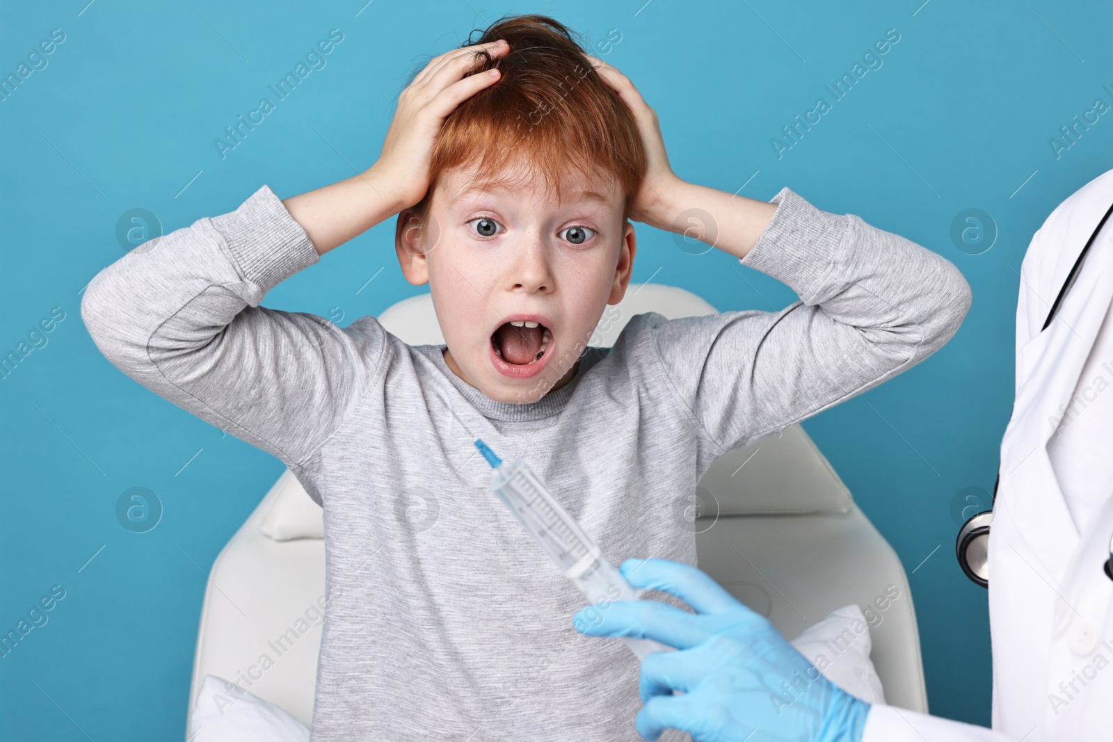 Photo of Dental phobia. Dentist with syringe near scared boy on light blue background