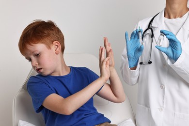 Dental phobia. Scared boy making stop gesture near dentist with syringe and vial on light grey background