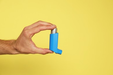 Photo of Man holding asthma inhaler on yellow background, closeup. Space for text