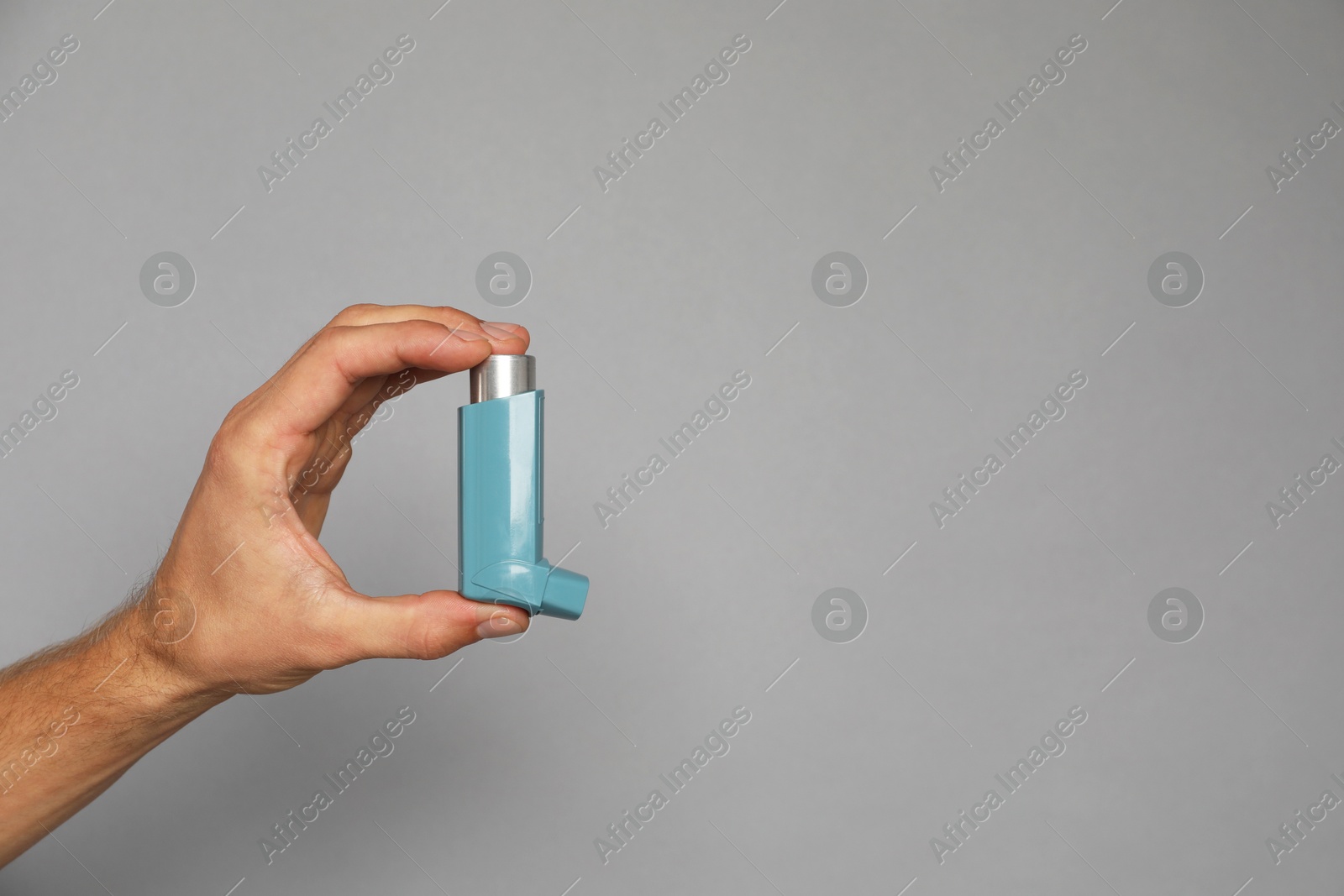 Photo of Man holding asthma inhaler on grey background, closeup. Space for text